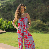 woman with brown hair wearing a jumpsuit with periwinkle background and bright red hibiscus print.
