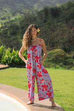 woman with brown hair wearing a jumpsuit with periwinkle background and bright red hibiscus print.