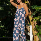 woman with black hair wearing a jumpsuit in a navy color with pink hibiscus blossoms 