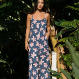 woman with black hair wearing a jumpsuit in a navy color with pink hibiscus blossoms 