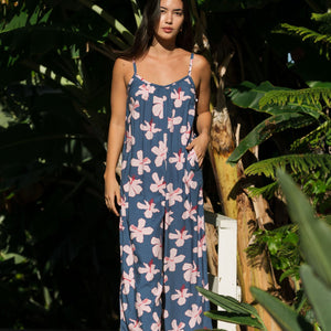 woman with black hair wearing a jumpsuit in a navy color with pink hibiscus blossoms 