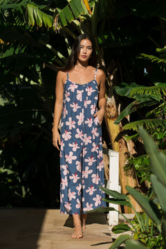 woman with black hair wearing a jumpsuit in a navy color with pink hibiscus blossoms 