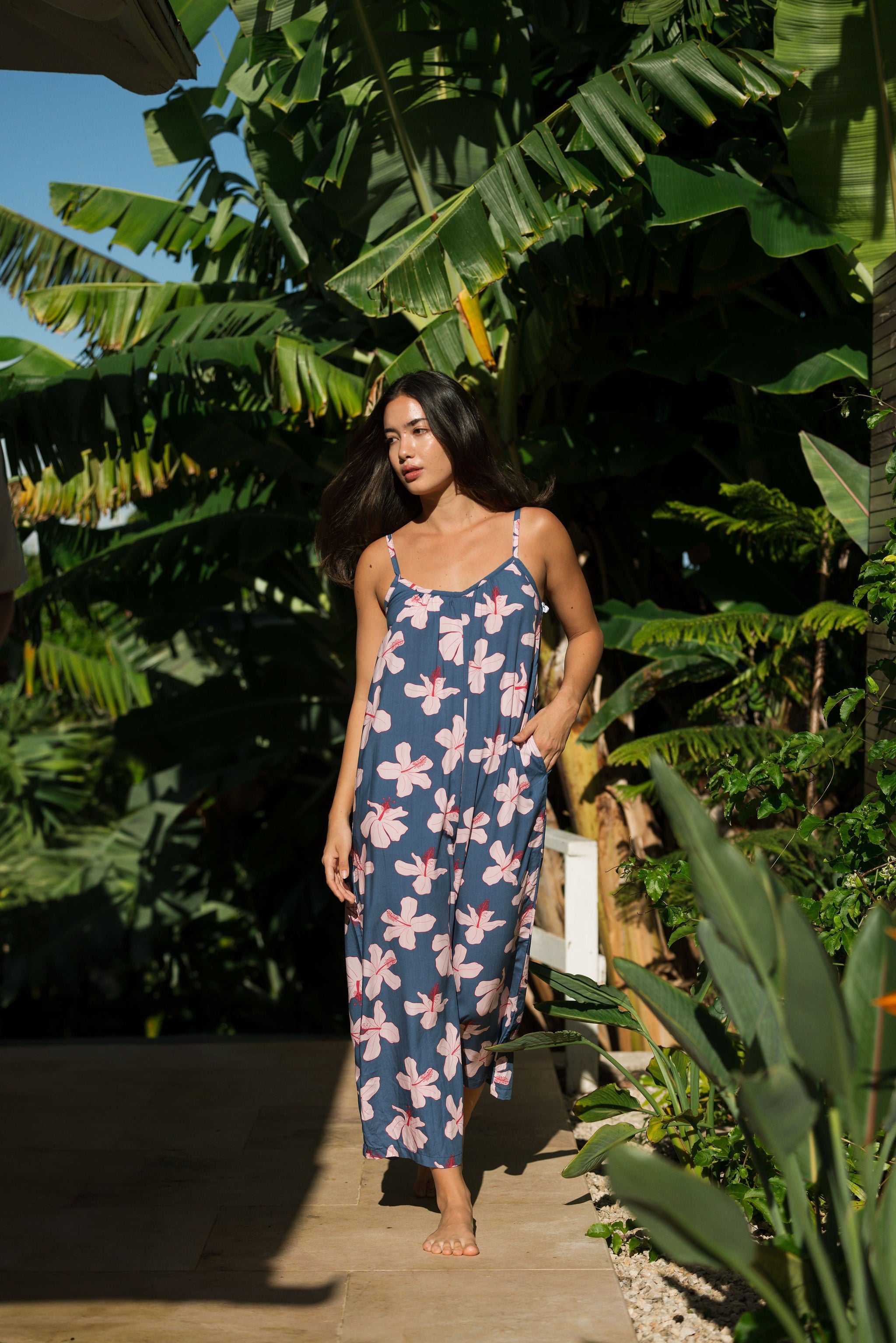 woman with black hair wearing a jumpsuit in a navy color with pink hibiscus blossoms 
