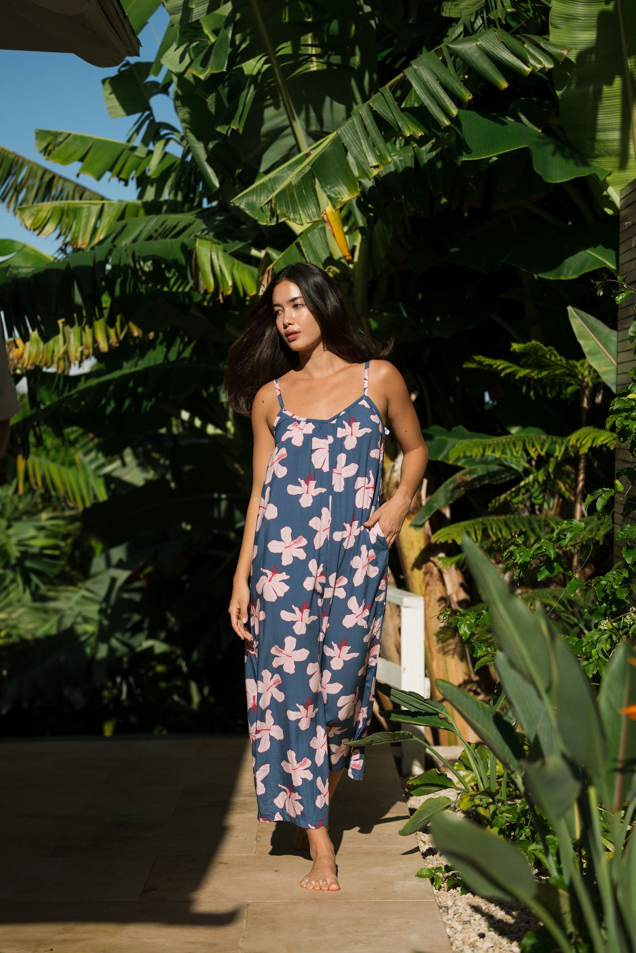 woman with black hair wearing a jumpsuit in a navy color with pink hibiscus blossoms 