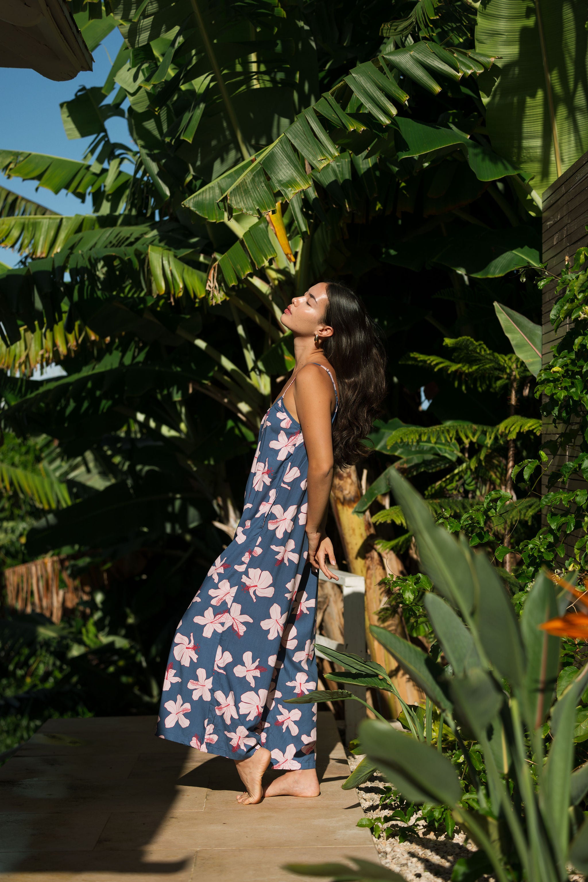 woman with black hair wearing a jumpsuit in a navy color with pink hibiscus blossoms 