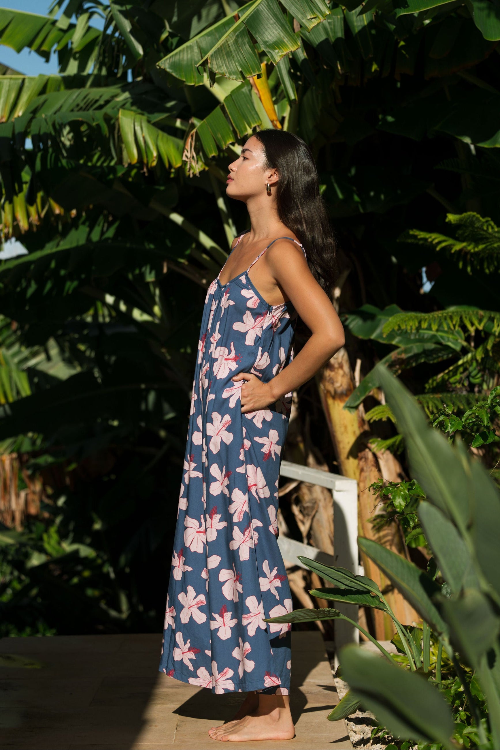 woman with black hair wearing a jumpsuit in a navy color with pink hibiscus blossoms 