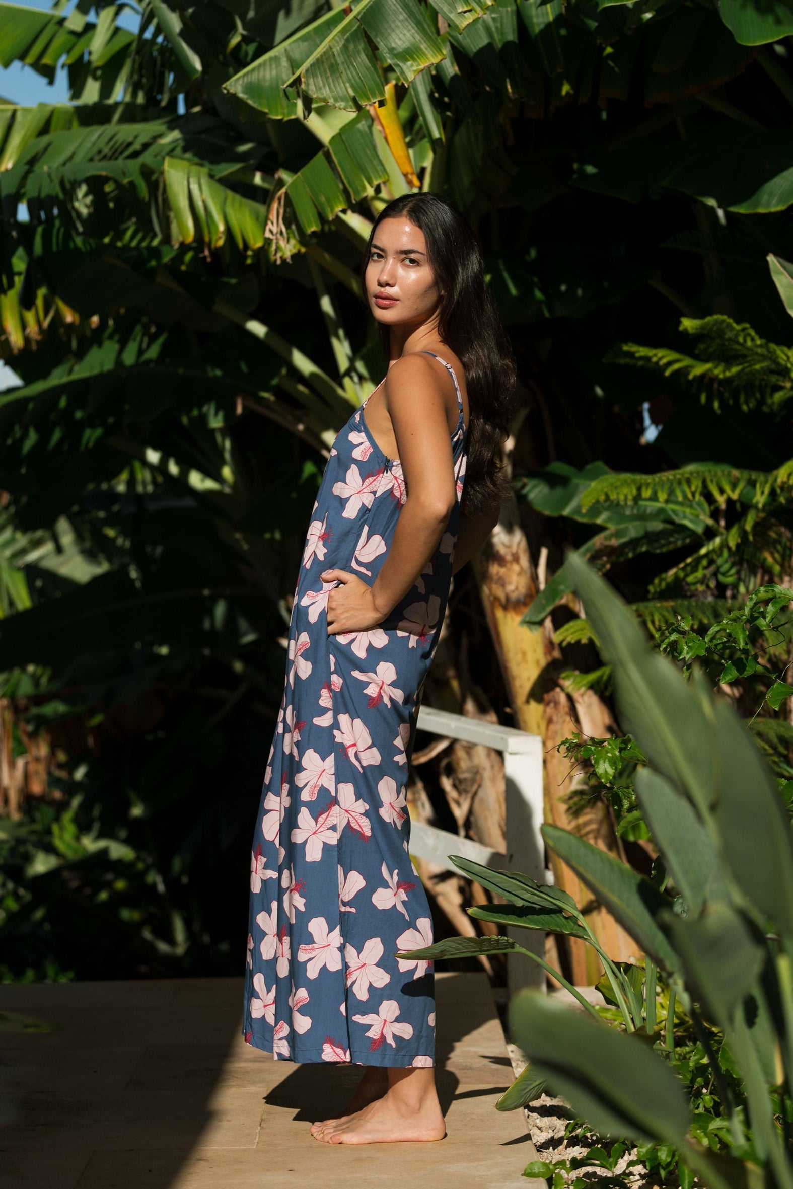 woman with black hair wearing a jumpsuit in a navy color with pink hibiscus blossoms 