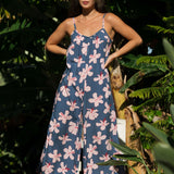 woman with black hair wearing a jumpsuit in a navy color with pink hibiscus blossoms 