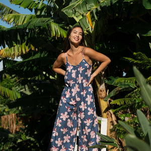 woman with black hair wearing a jumpsuit in a navy color with pink hibiscus blossoms 