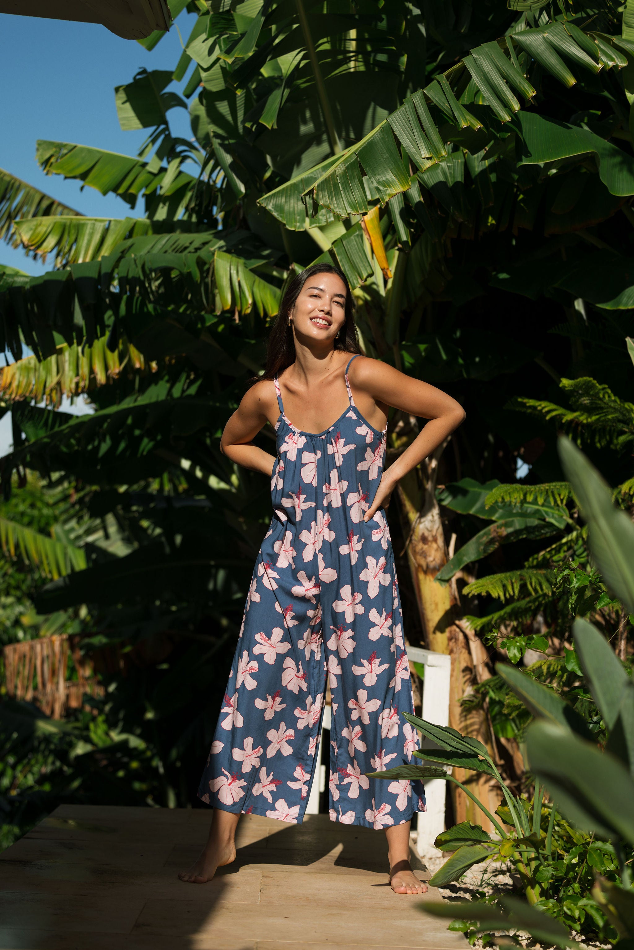 woman with black hair wearing a jumpsuit in a navy color with pink hibiscus blossoms 