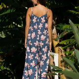 woman with black hair wearing a jumpsuit in a navy color with pink hibiscus blossoms 