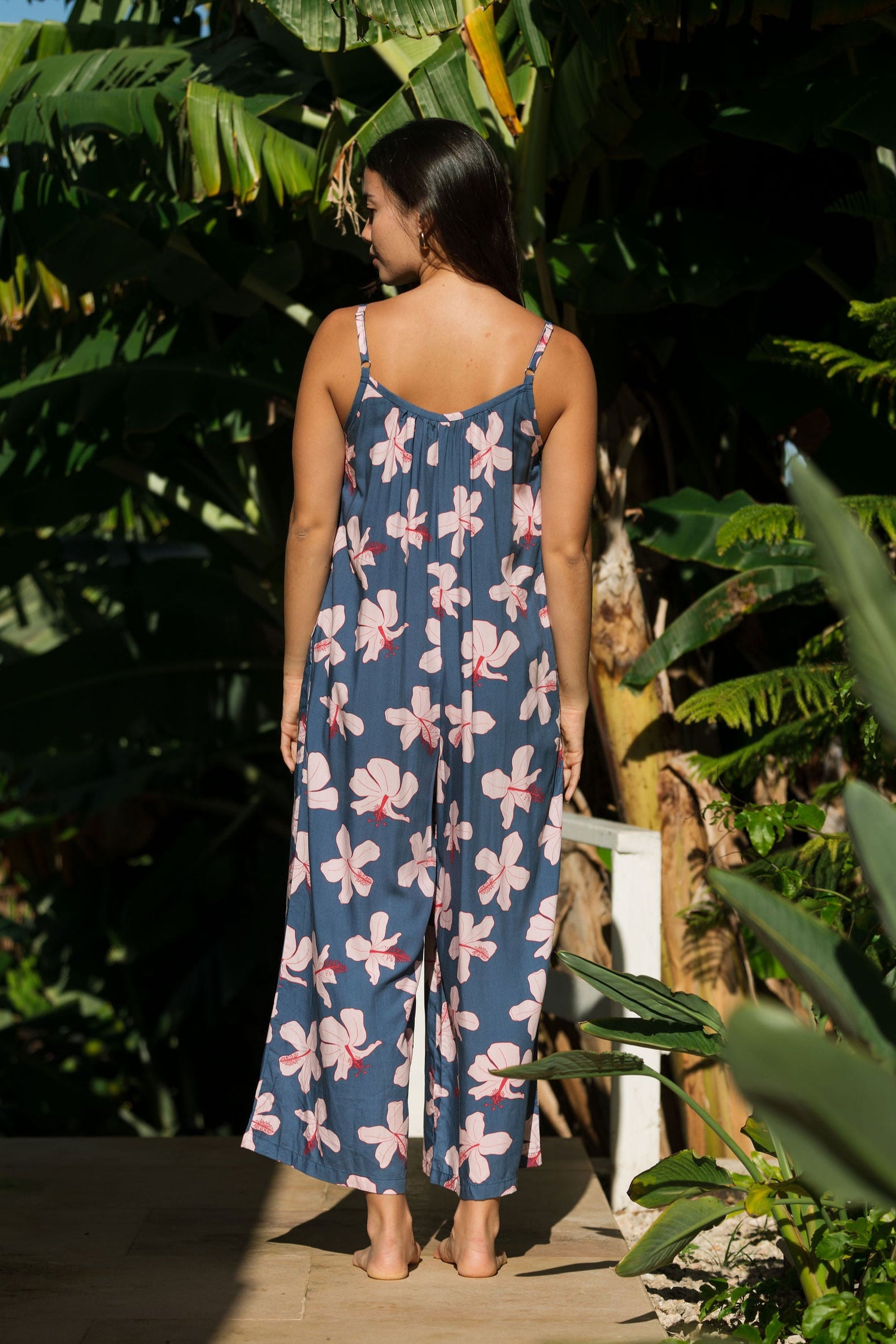 woman with black hair wearing a jumpsuit in a navy color with pink hibiscus blossoms 