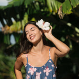woman with black hair wearing a jumpsuit in a navy color with pink hibiscus blossoms 