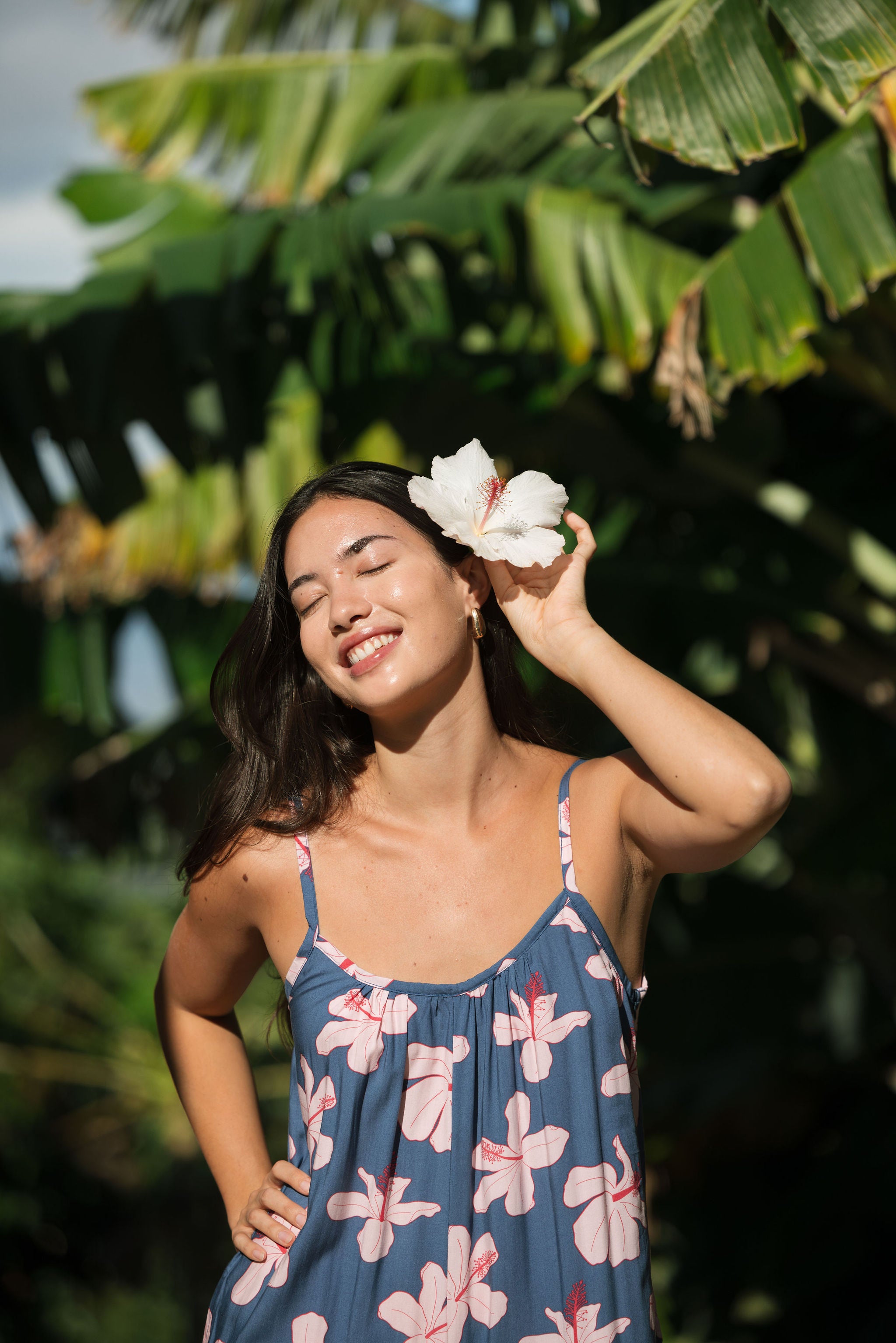 woman with black hair wearing a jumpsuit in a navy color with pink hibiscus blossoms 