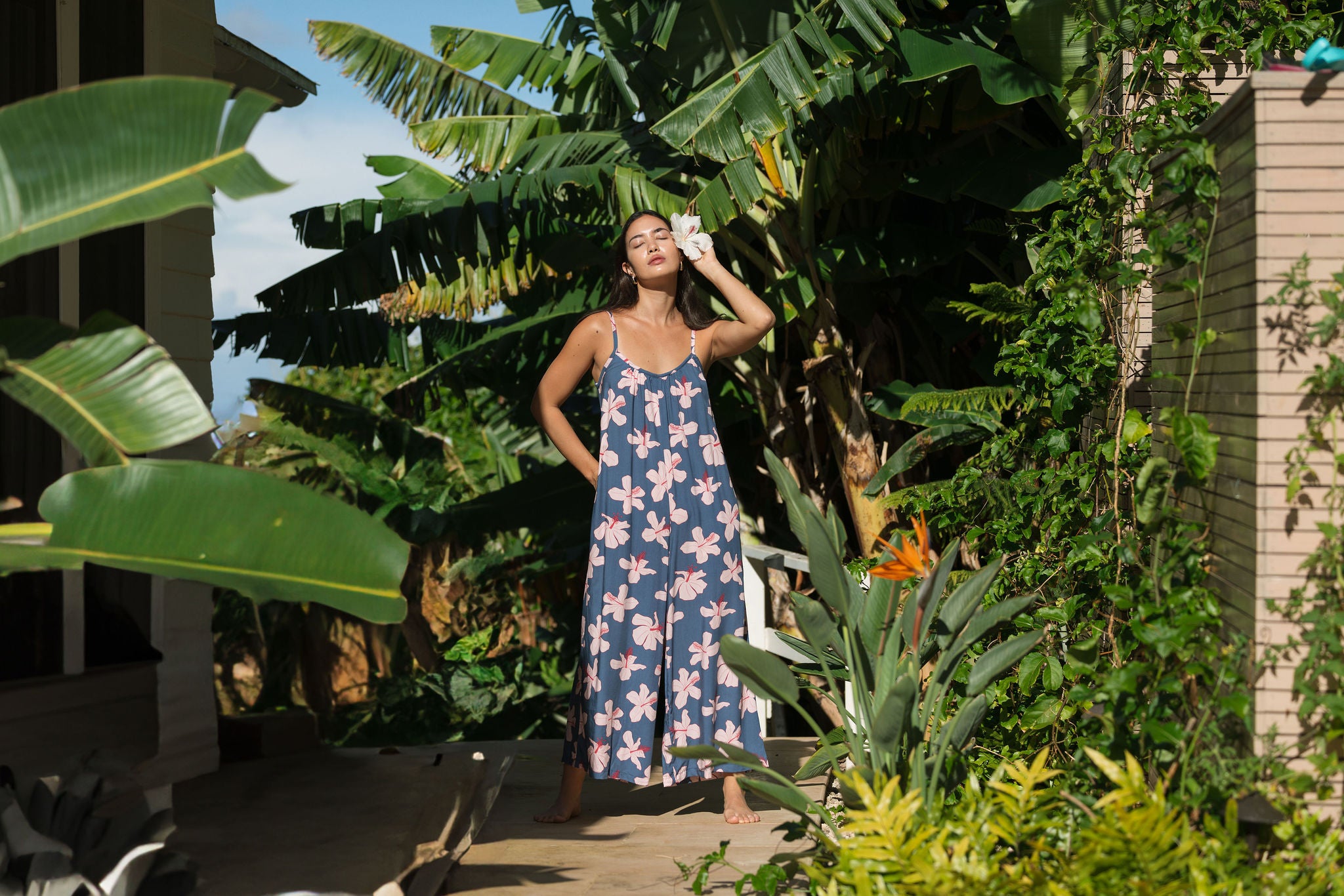 woman with black hair wearing a jumpsuit in a navy color with pink hibiscus blossoms 