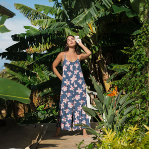 woman with black hair wearing a jumpsuit in a navy color with pink hibiscus blossoms 