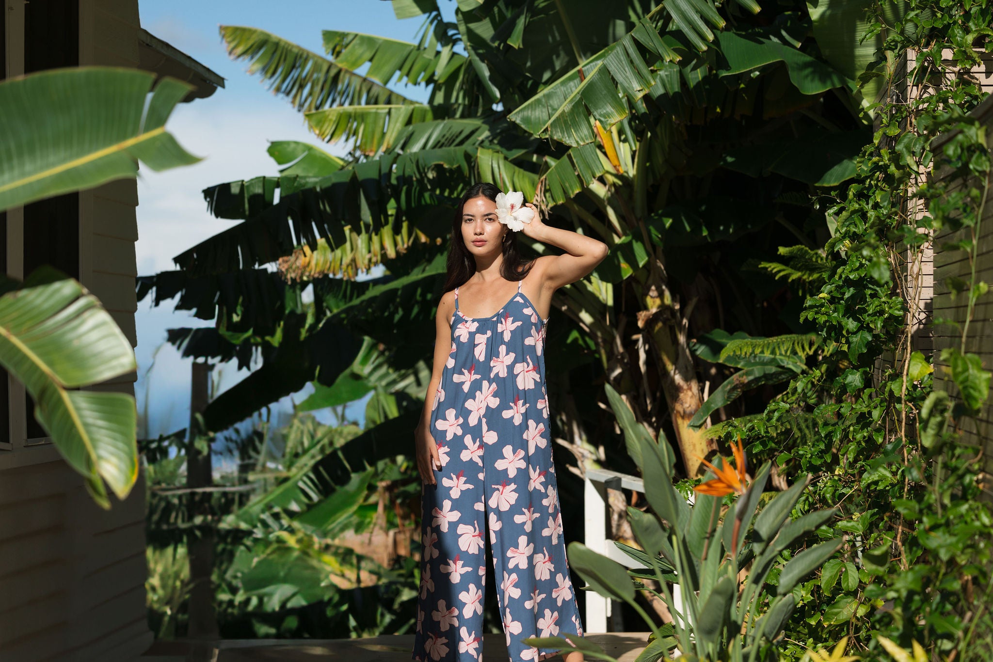 woman with black hair wearing a jumpsuit in a navy color with pink hibiscus blossoms 