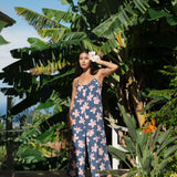 woman with black hair wearing a jumpsuit in a navy color with pink hibiscus blossoms 
