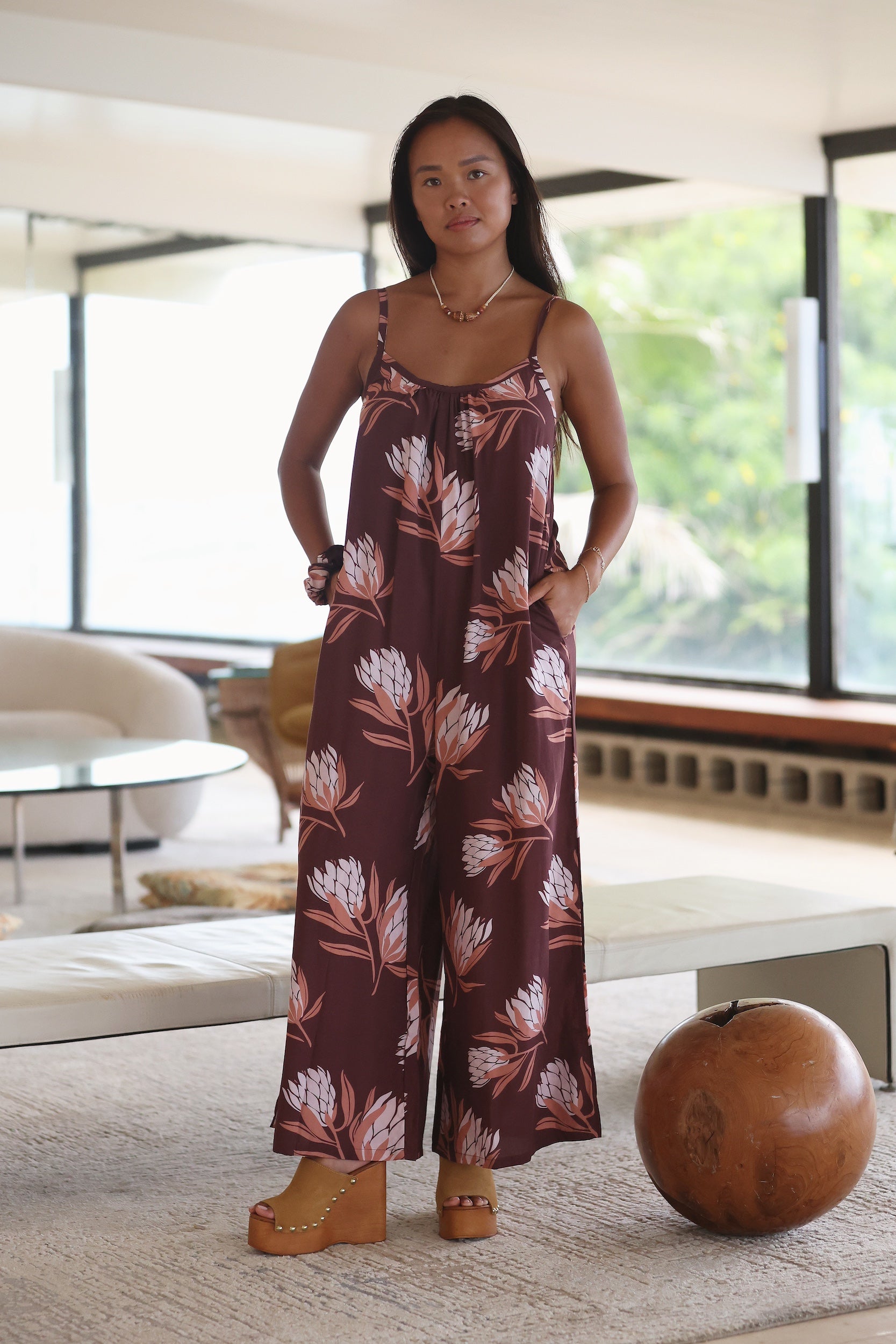 woman wearing simple brown spaghetti strap jumpsuit with protea print