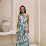 woman with brown hair wearing tiered halter maxi dress in teal with large cream colored orchids.