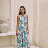 woman with brown hair wearing tiered halter maxi dress in teal with large cream colored orchids.