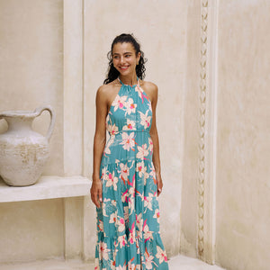 woman with brown hair wearing tiered halter maxi dress in teal with large cream colored orchids.