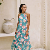 woman with brown hair wearing tiered halter maxi dress in teal with large cream colored orchids.