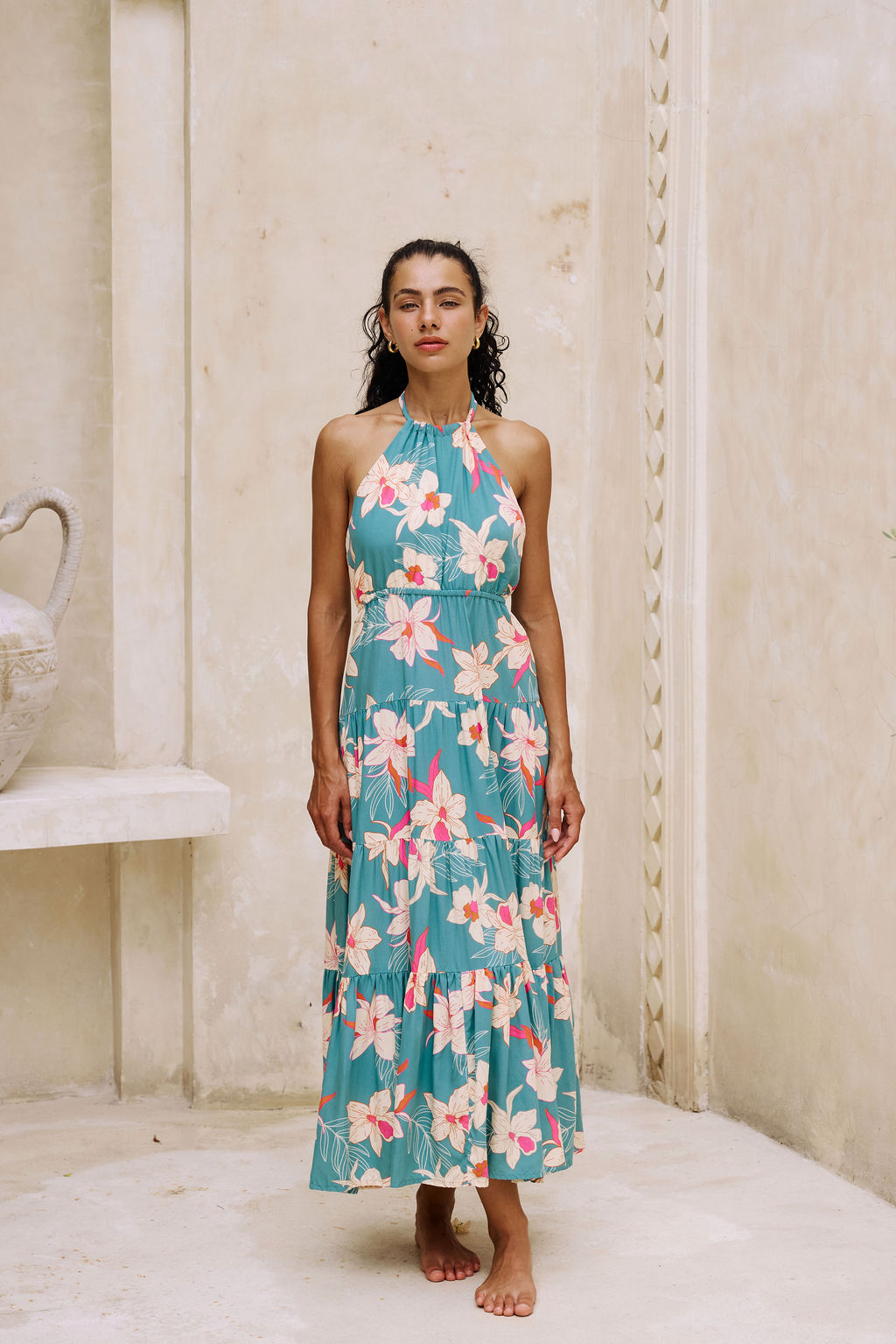 woman with brown hair wearing tiered halter maxi dress in teal with large cream colored orchids.
