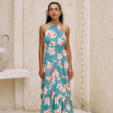 woman with brown hair wearing tiered halter maxi dress in teal with large cream colored orchids.