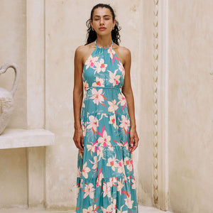 woman with brown hair wearing tiered halter maxi dress in teal with large cream colored orchids.