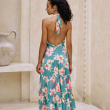 woman with brown hair wearing tiered halter maxi dress in teal with large cream colored orchids.
