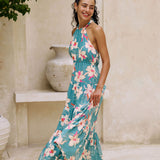 woman with brown hair wearing tiered halter maxi dress in teal with large cream colored orchids.