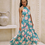 woman with brown hair wearing tiered halter maxi dress in teal with large cream colored orchids.