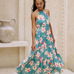 woman with brown hair wearing tiered halter maxi dress in teal with large cream colored orchids.