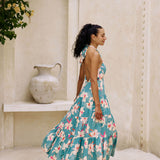 woman with brown hair wearing tiered halter maxi dress in teal with large cream colored orchids.