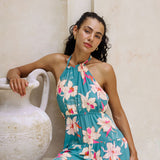 woman with brown hair wearing tiered halter maxi dress in teal with large cream colored orchids.