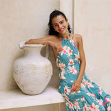 woman with brown hair wearing tiered halter maxi dress in teal with large cream colored orchids.