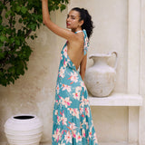 woman with brown hair wearing tiered halter maxi dress in teal with large cream colored orchids.