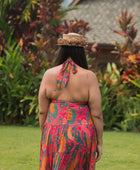 woman with brown hair wearing a colorful flowy maxi dress with tropical lei print