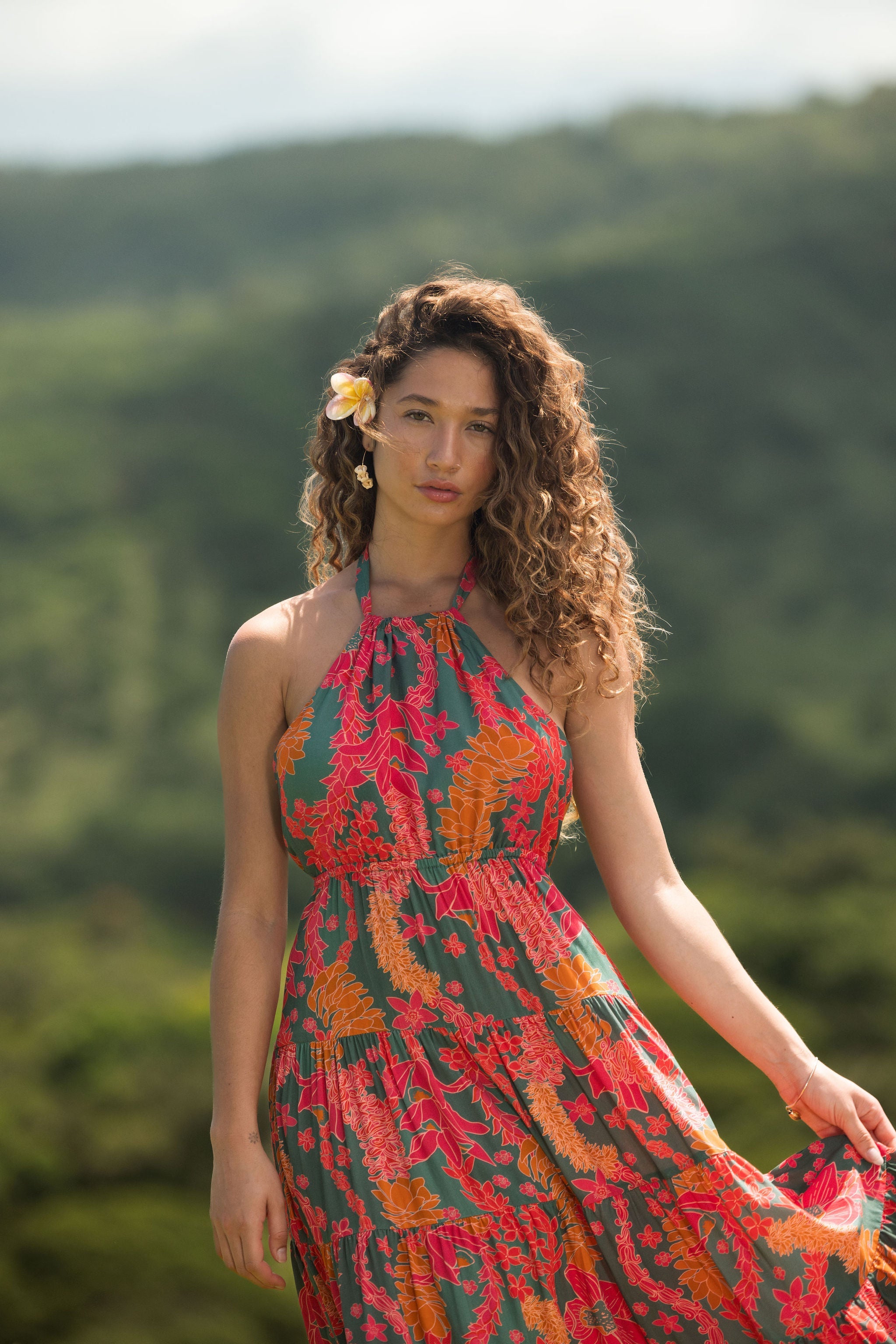 woman with brown hair wearing a colorful flowy maxi dress with tropical lei print