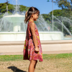 little girl wearing terracotta colored high neck sleeveless knee length dress with large purple and yellow flower print
