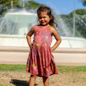 little girl wearing terracotta colored high neck sleeveless knee length dress with large purple and yellow flower print