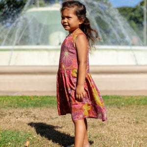 little girl wearing terracotta colored high neck sleeveless knee length dress with large purple and yellow flower print