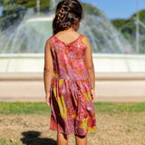 little girl wearing terracotta colored high neck sleeveless knee length dress with large purple and yellow flower print