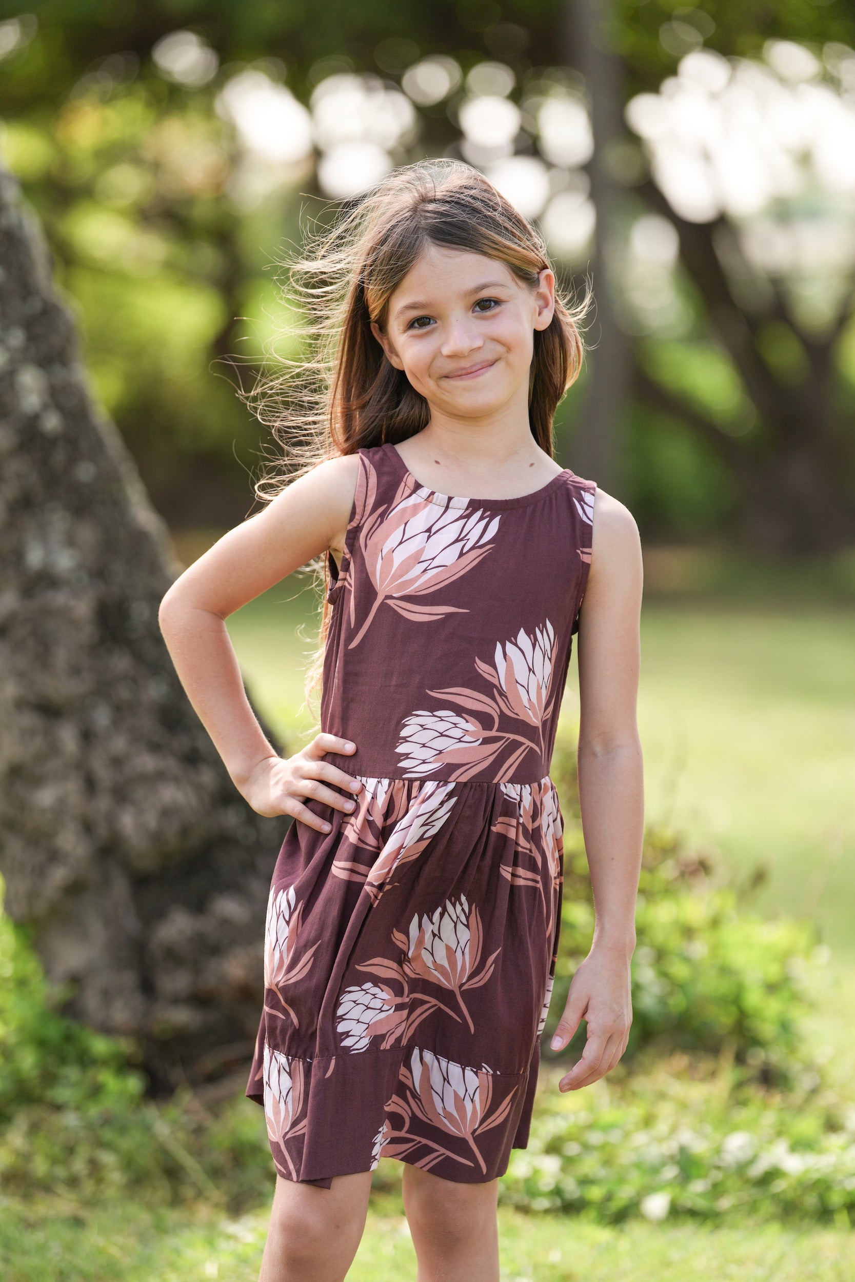 little girl wearing brown high neck, sleeveless dress with protea print