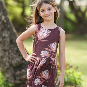 little girl wearing brown high neck, sleeveless dress with protea print
