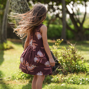 little girl wearing brown high neck, sleeveless dress with protea print