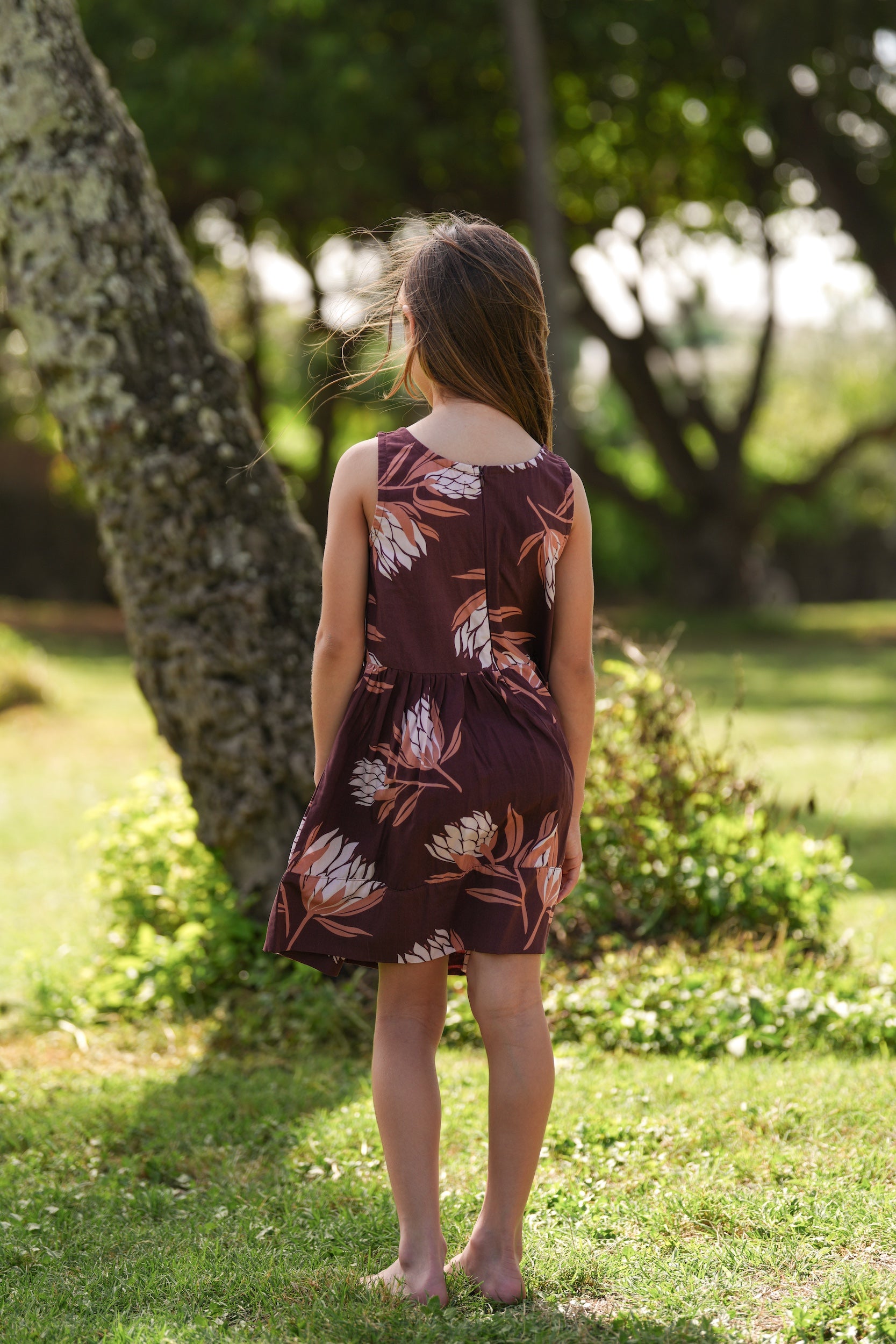 little girl wearing brown high neck, sleeveless dress with protea print