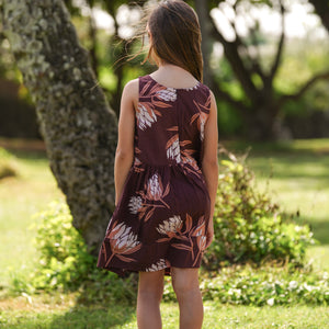 little girl wearing brown high neck, sleeveless dress with protea print