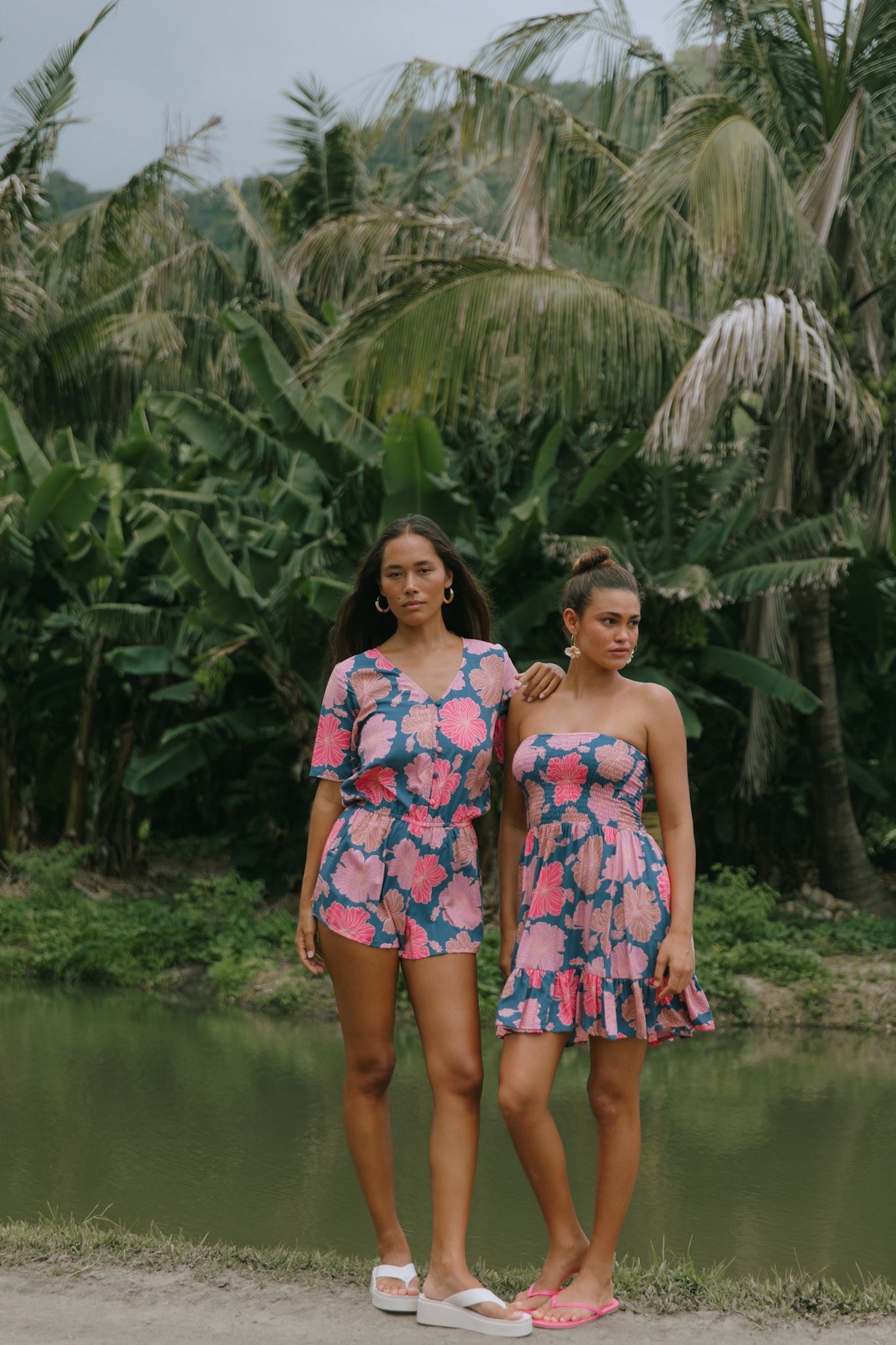 woman with brown hair wearing a navy playsuit with bright pink hibiscus print
